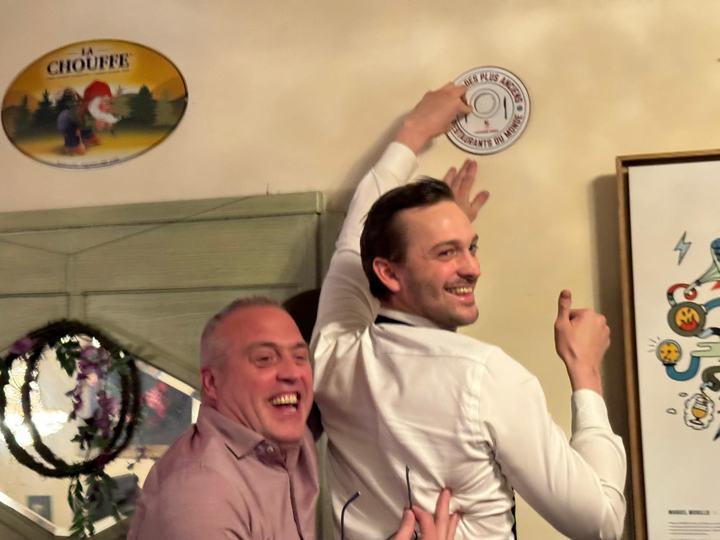 Een ober drukt het schild tegen de muur naast een bord van La Chouffe en steekt lachend zijn duim op