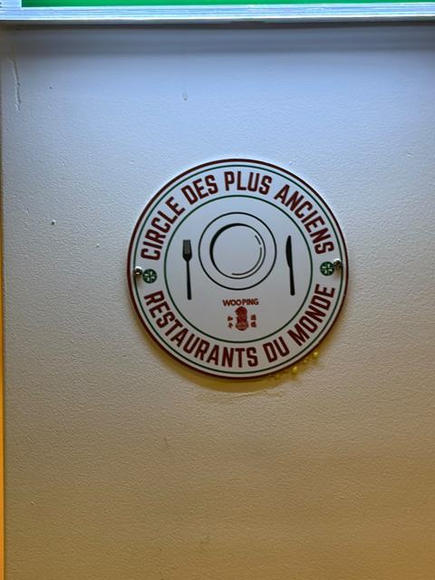 Het schild van de Cercle met in het midden het logo van Woo Ping, vastgeschroefd aan een lichte wand